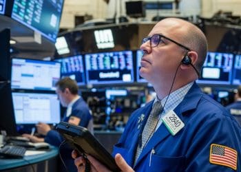 A stock trader shows concern while watching market data decline on electronic screens, illustrating the financial impact of tariffs.