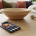 High angle close up of Google Pixel 10 Pro in Obsidian on a light wood coffee table next to a decorative bowl with a sleeping dog on a sofa in the background.