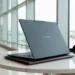 Rear view of an open Lenovo Yoga Slim 7x in Cosmic Blue on a marble table in a sunlit airport lounge.