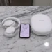 White Bose over-ear headphones resting on a marble countertop next to a smartphone displaying the Bose Music app and a white hard-shell carrying case.